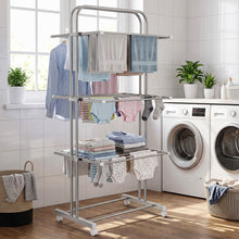 A stainless steel 3-layer clothes drying rack with various clothes and towels, positioned in a laundry room with washing