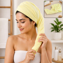 A woman with a yellow microfiber hair wrap towel on her head, holding the twisted end.