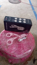 A pink electric eyelash curler and its dark blue box rest on a pink wrapped stool on a tiled floor.