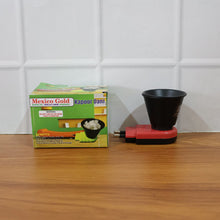 A red and black electric Kapoor Dani diffuser next to its green and yellow product packaging on a wooden surface.