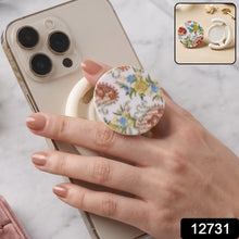 A hand holds a white smartphone with a round pop socket featuring a white background and colorful paisley floral pattern.