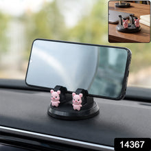 A black phone holder with two pink pig figurines on a car dashboard, holding a smartphone horizontally.