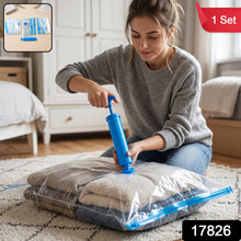 A woman kneels on a rug, using a blue hand pump to compress clothes inside a clear vacuum storage bag. A red label says '1