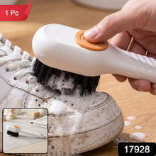 A person uses a white and orange scrubbing brush to clean a dirty white sneaker, creating soap suds.