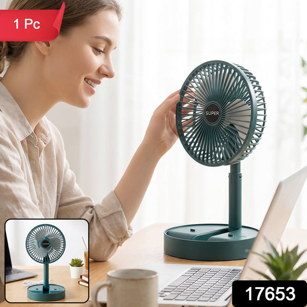 A dark green portable fan with a white USB cable on a wooden desk with a laptop and iced tea.
