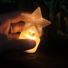 A hand holding a single glowing LED tealight with a golden mesh star in a dimly lit setting.
