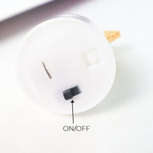 Close-up of the bottom of a white LED tealight, showing the black on/off switch with an arrow.